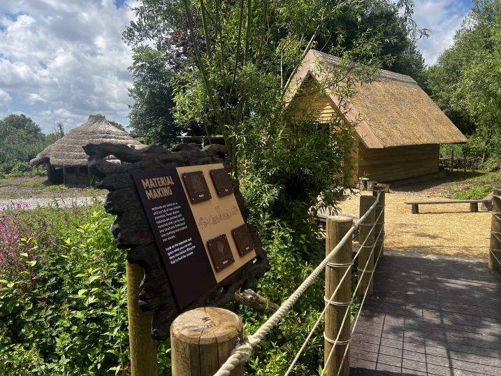 Shows the end of the boardwalk before reaching the longhouse. In the photo is a sign with information about making materials using wetlands.